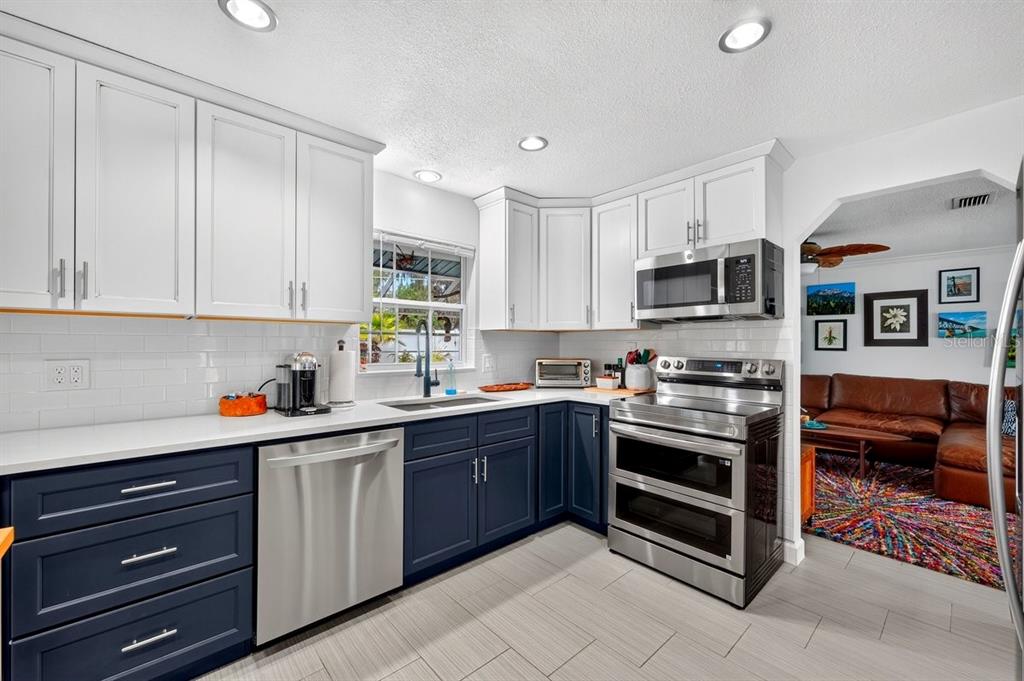 A kitchen features white upper cabinets, dark blue lower cabinets, stainless steel appliances, and tile flooring — 237 BRITTANY AVENUE, PORT ORANGE, FL