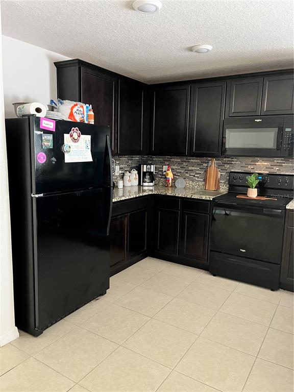 A kitchen features dark wood cabinets, granite countertops, black appliances, and light-colored tile flooring — 2121 HIBISCUS PLACE, KISSIMMEE, FL