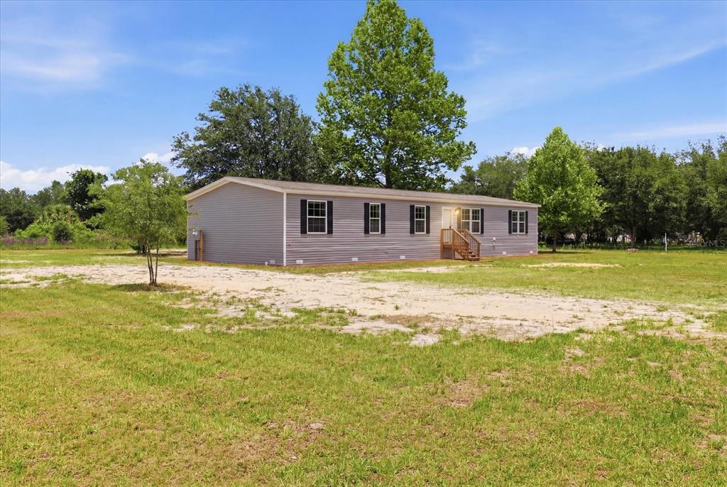 A single-story manufactured home with gray siding sits on a large, grassy lot — 11975 NE 227TH PLACE, FORT MC COY, FL