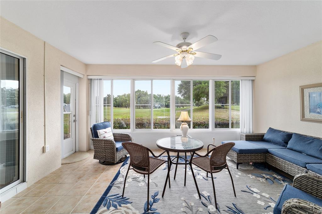 A sunroom features tile floors, wicker furniture, a ceiling fan, and views of a golf course — 13640 SW 115TH AVENUE, DUNNELLON, FL