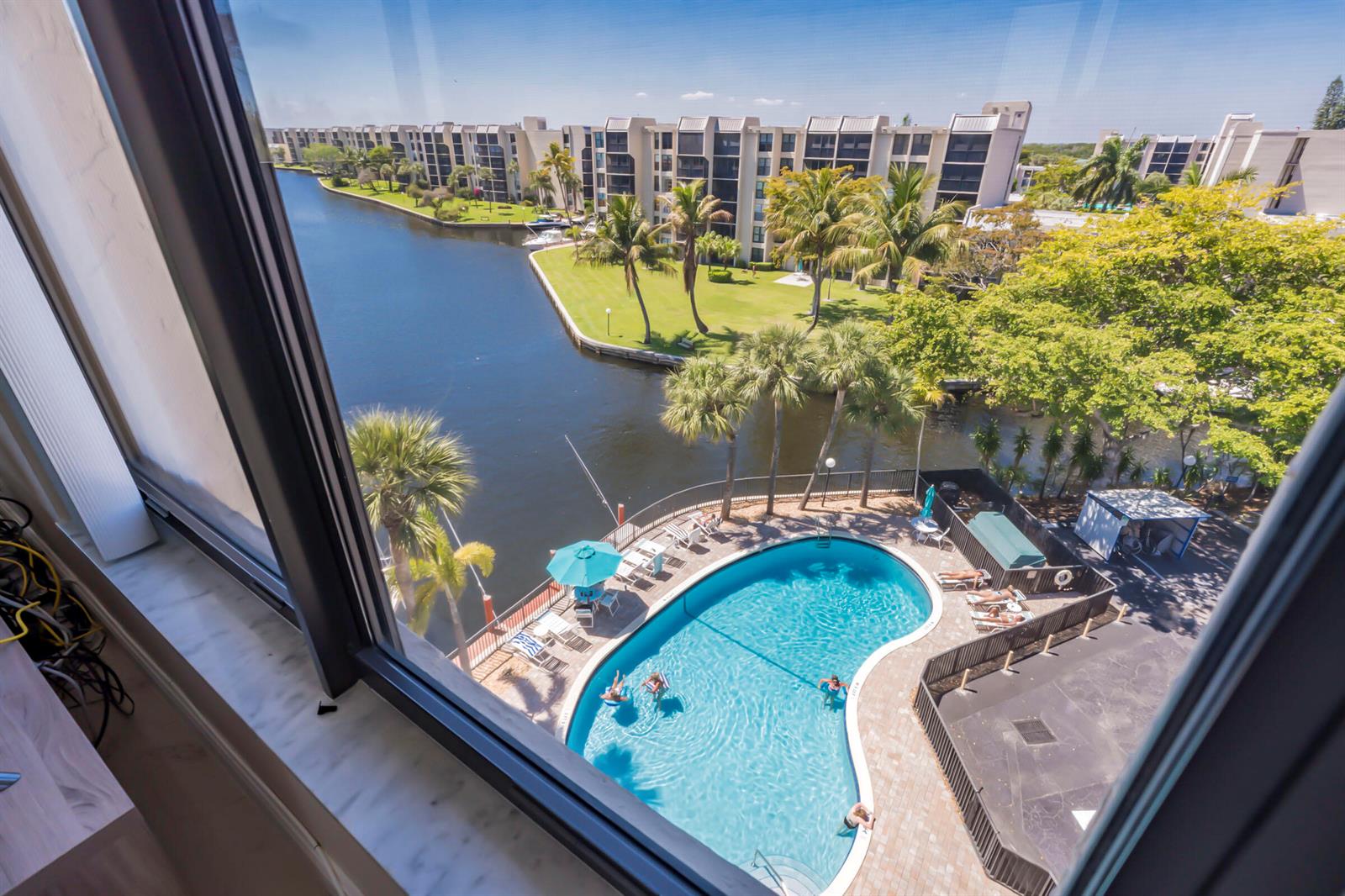 A high-angle view from a window overlooks a swimming pool, canal, and apartment buildings — 22 Royal Palm Way # 606, Boca Raton FL 33432, BOCA RATON, FL