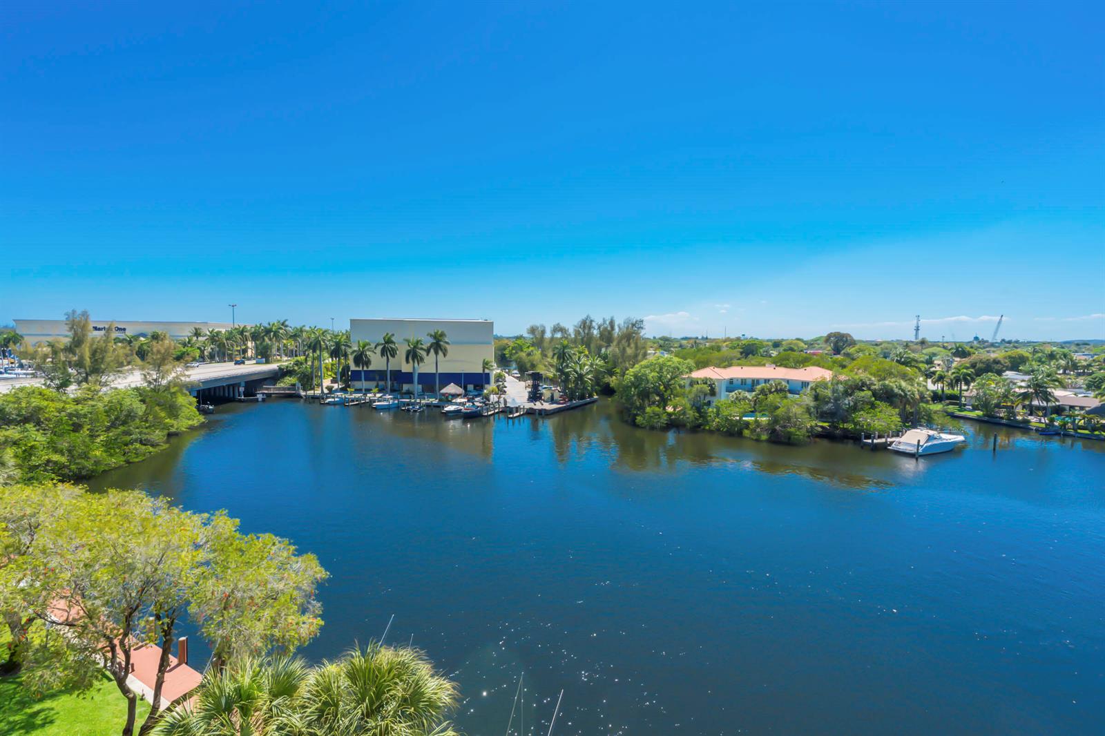 An aerial view shows a canal with boats, palm trees, a bridge, and nearby buildings — 22 Royal Palm Way # 606, Boca Raton FL 33432, BOCA RATON, FL