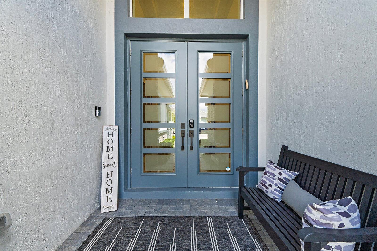 A blue double front door with glass panels sits on a porch with a bench — 12172 Waterstone Circle, Palm Beach Gardens FL 33412, PALM BEACH GARDENS, FL