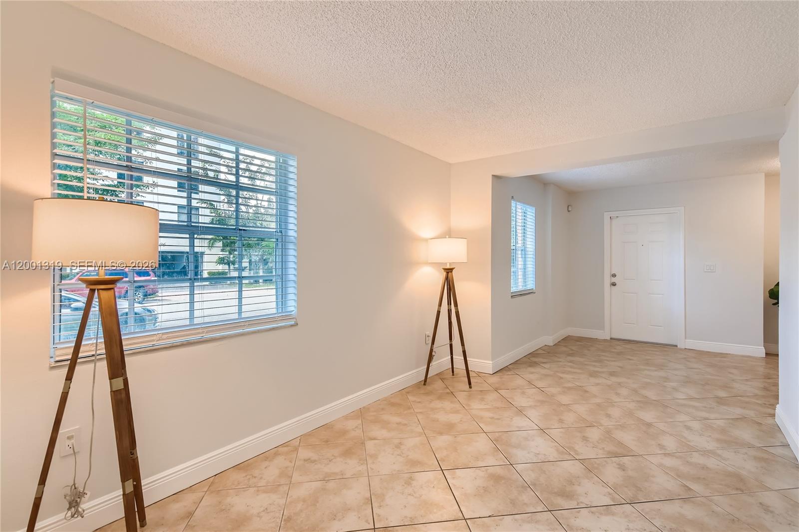 An empty room features beige tile flooring, two tripod floor lamps, and a white door — 29 Santillane Ave # 2, Coral Gables FL 33134, CORAL GABLES, FL