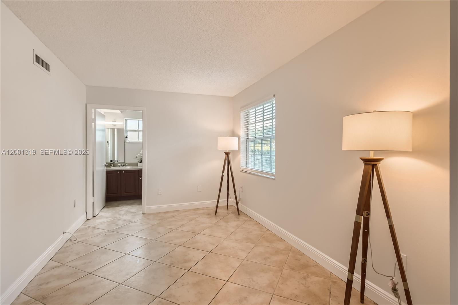 This room features beige tile flooring, light-colored walls, two tripod floor lamps, and a bathroom — 29 Santillane Ave # 2, Coral Gables FL 33134, CORAL GABLES, FL