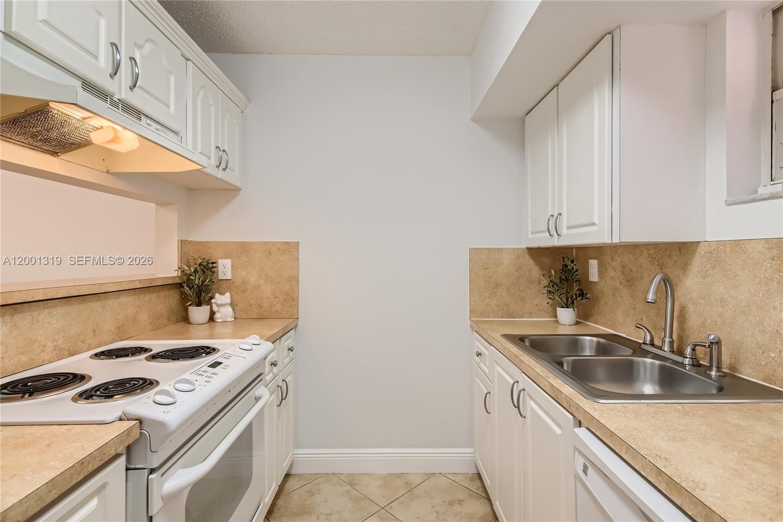 A galley kitchen features white cabinets, tan countertops, a stove, and a double sink — 29 Santillane Ave # 2, Coral Gables FL 33134, CORAL GABLES, FL