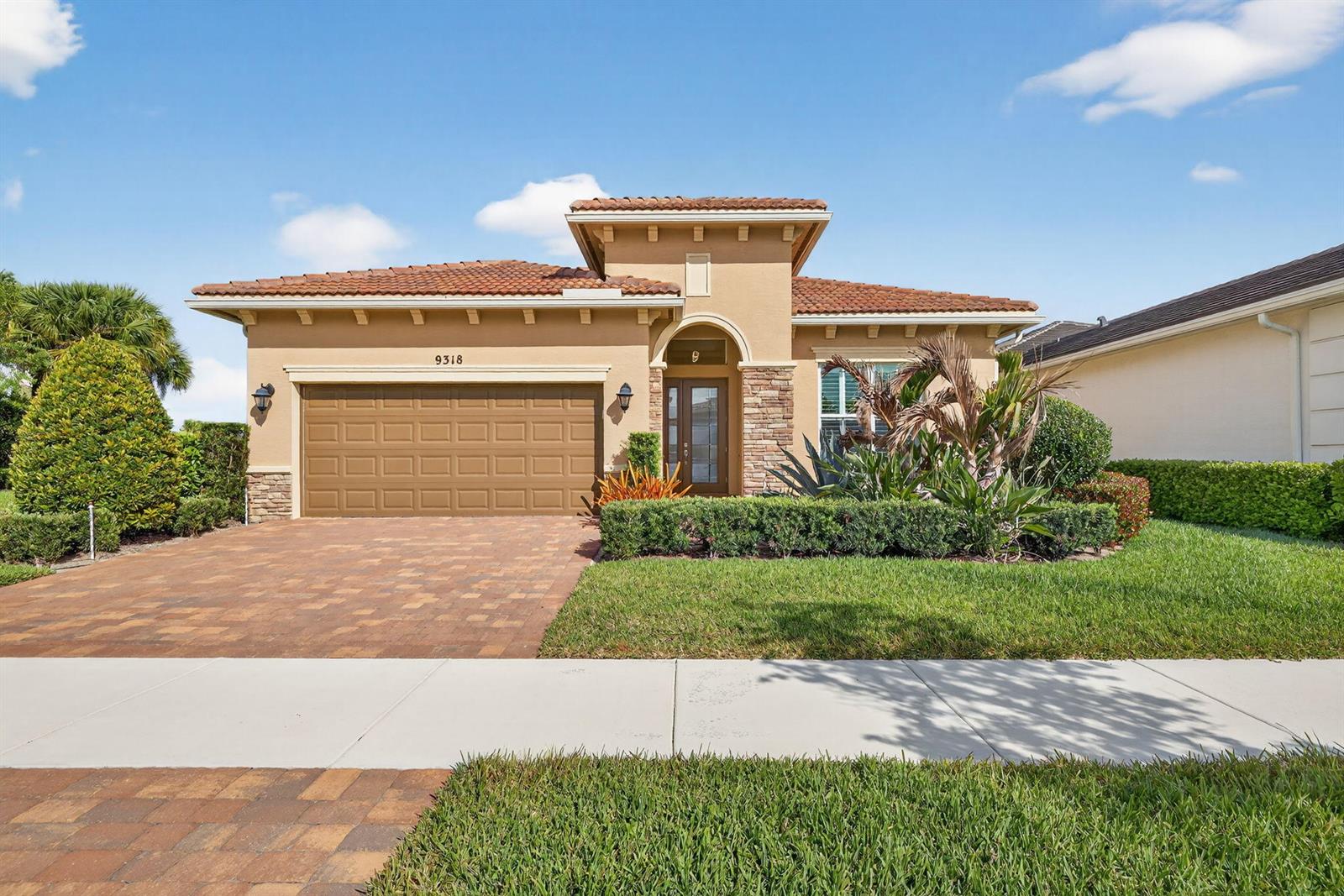 A single-story house with a tan stucco exterior, tile roof, and a paved driveway — 9318 SW Miracoli Way, Port St. Lucie FL 34987, PORT ST. LUCIE, FL