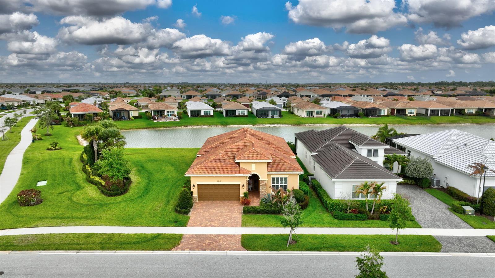 An aerial view shows a tan house with a tiled roof facing a neighborhood pond — 9318 SW Miracoli Way, Port St. Lucie FL 34987, PORT ST. LUCIE, FL