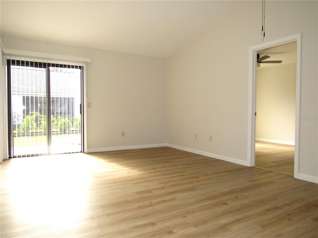 An empty room with light wood-look flooring, a sliding glass door, and an open doorway — 20005 GOLDCUP COURT, PORT CHARLOTTE, FL