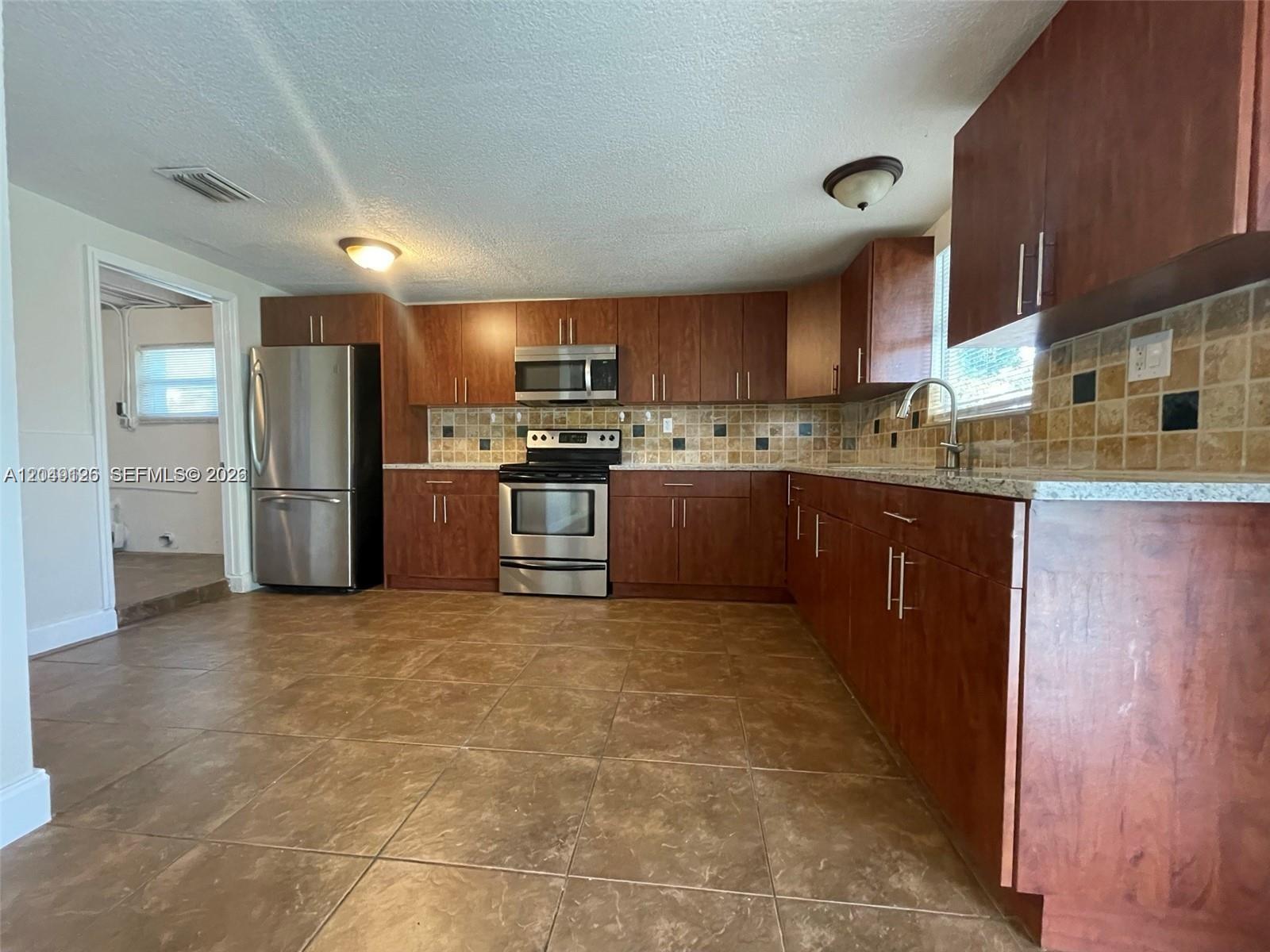 A kitchen features dark wood cabinets, stainless steel appliances, and brown tiled flooring — 4160 SW 36th St, West Park FL 33023, WEST PARK, FL
