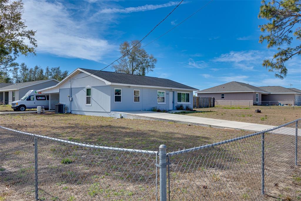 A light blue single-story house with a carport and a chain-link fence in the yard — 9782 SE 157TH LANE, SUMMERFIELD, FL