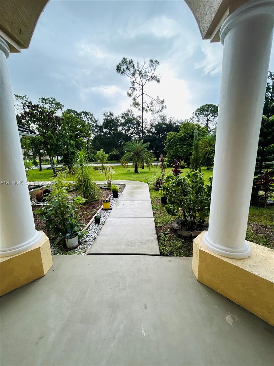A concrete walkway leads through a landscaped yard between two white porch columns — 13754 N 48th Ct N, West Palm Beach FL 33411, WEST PALM BEACH, FL