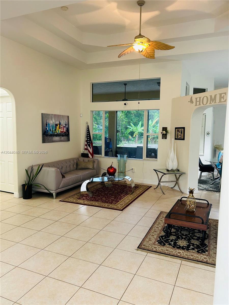 A living room features tile flooring, a tray ceiling with a fan, and large windows — 13754 N 48th Ct N, West Palm Beach FL 33411, WEST PALM BEACH, FL