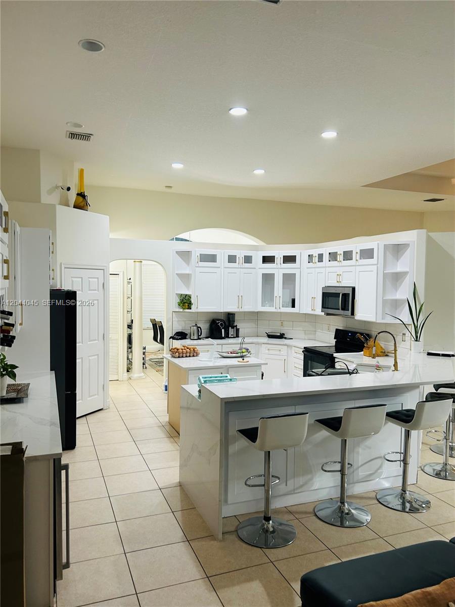 A white kitchen features a central island, breakfast bar seating, and light-colored tile flooring — 13754 N 48th Ct N, West Palm Beach FL 33411, WEST PALM BEACH, FL