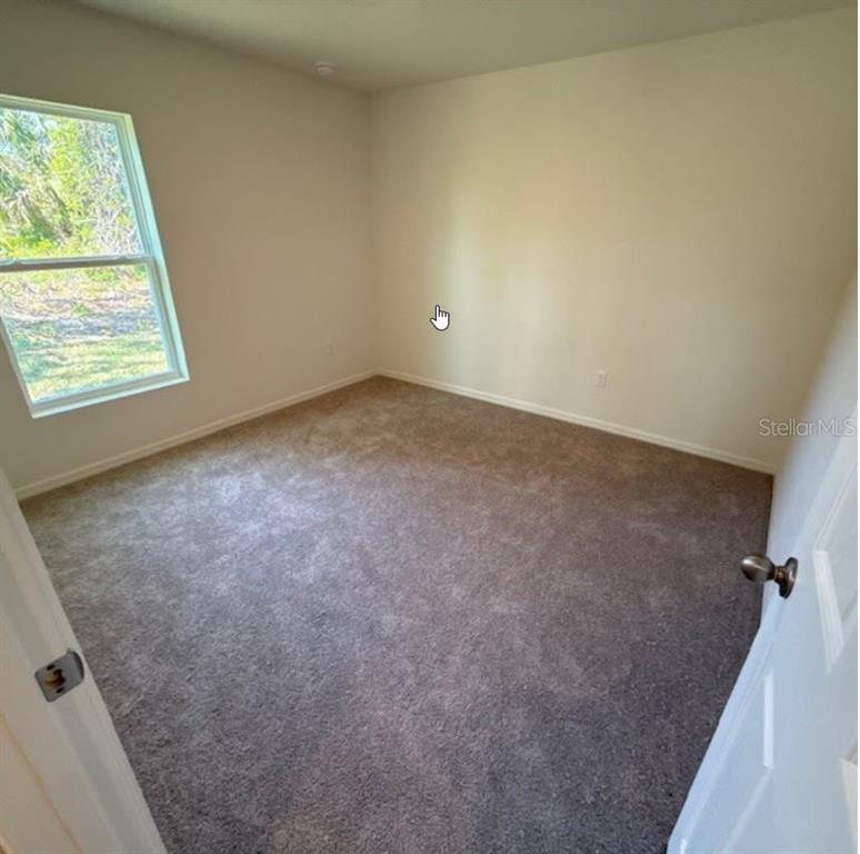 An empty bedroom with beige walls, gray carpet, and a single window — 37 PACKARD LANE, PALM COAST, FL