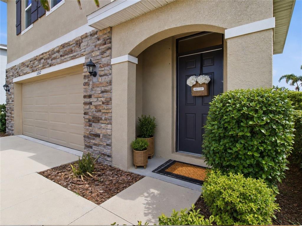 The exterior of a house features a stone-accented garage, a dark front door, and landscaping — 3262 HILLTOP CIRCLE, BRADENTON, FL
