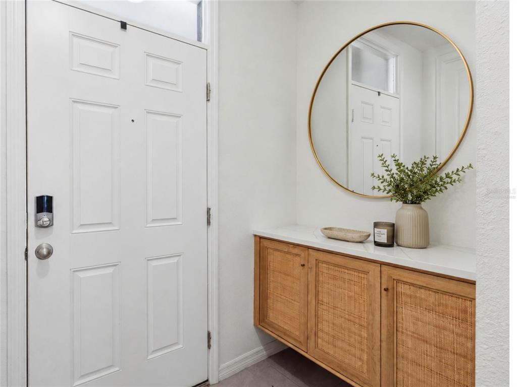 An entryway features a white door, a round gold mirror, and a wood-accented floating console — 3262 HILLTOP CIRCLE, BRADENTON, FL
