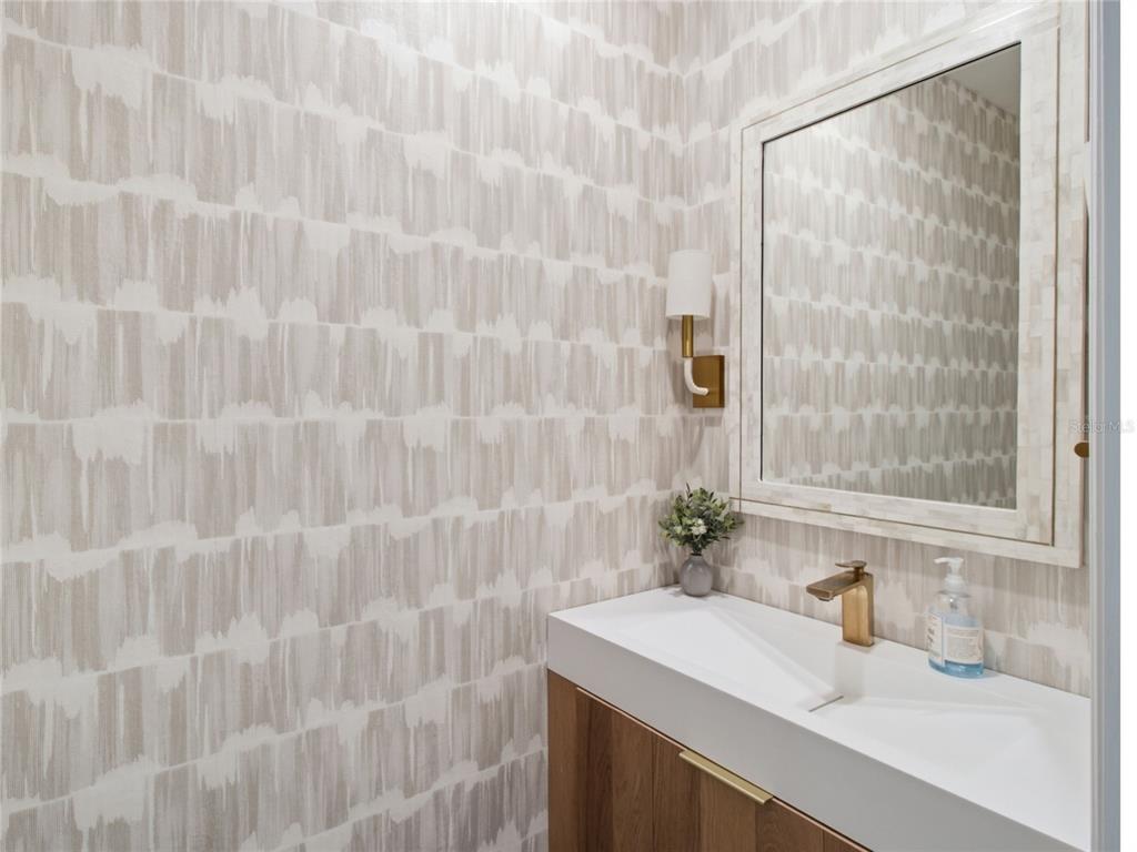 A modern powder room features patterned wallpaper, a wood vanity, and a brass faucet — 3262 HILLTOP CIRCLE, BRADENTON, FL