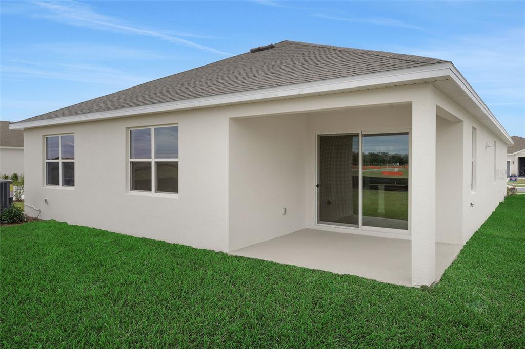 The exterior rear view of a house features a covered patio and a sliding glass door — 4117 PENELOPE AVENUE, LAKE WALES, FL
