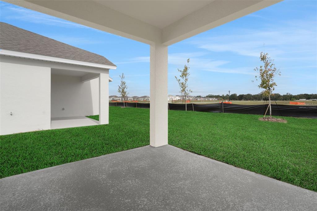 A covered concrete patio overlooks a grassy backyard with a black construction fence — 4117 PENELOPE AVENUE, LAKE WALES, FL