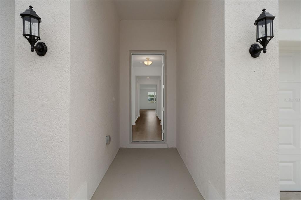 A covered entryway with two wall-mounted lanterns leads to an open doorway revealing interior hallways — 4117 PENELOPE AVENUE, LAKE WALES, FL