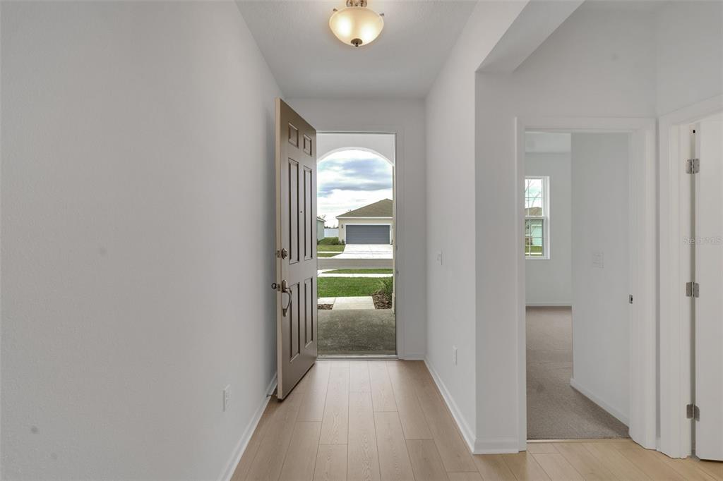 An entryway with light wood flooring leads to an open front door showing a neighborhood — 4117 PENELOPE AVENUE, LAKE WALES, FL