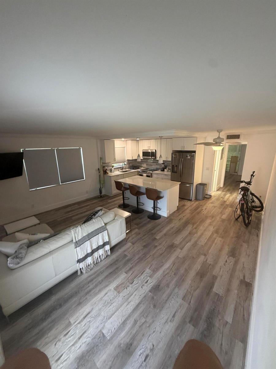 An open-concept living room and kitchen featuring white cabinets, a central island, and wood-look flooring — 209 Newport M # 209, Deerfield Beach FL 33442, DEERFIELD BEACH, FL