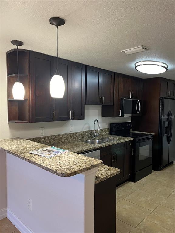 A kitchen features dark wood cabinets, granite countertops, stainless steel appliances, and two pendant lights — 15532 CHAMBERLAIN BOULEVARD UNIT A, PORT CHARLOTTE, FL