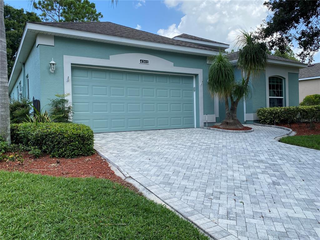 A teal house with a two-car garage and a paved driveway under a blue sky — 4202 HAMMERSMITH DRIVE, CLERMONT, FL