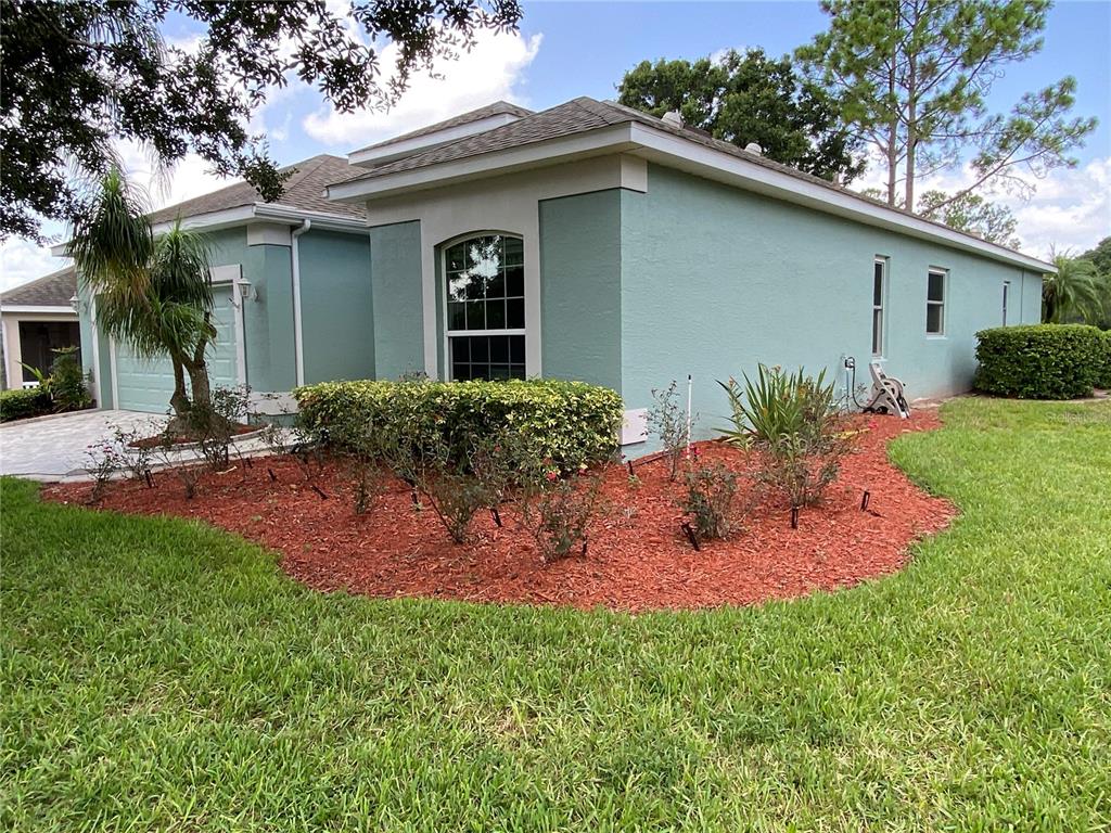 A light blue house exterior features a front garden bed with red mulch and shrubs — 4202 HAMMERSMITH DRIVE, CLERMONT, FL