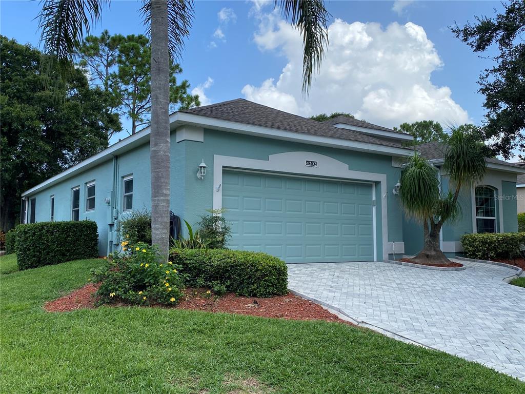 A teal, single-story house features a two-car garage, a paved driveway, and palm trees — 4202 HAMMERSMITH DRIVE, CLERMONT, FL
