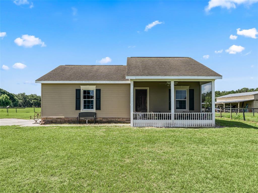 A tan single-story house features a front porch with a white railing and black shutters — 2223 CR 543, SUMTERVILLE, FL