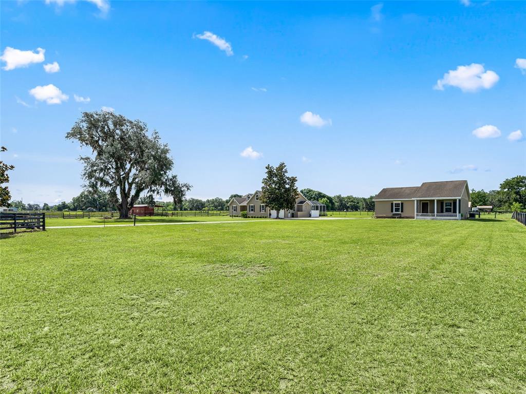 A large grassy field features two houses and a large tree under a blue sky — 2223 CR 543, SUMTERVILLE, FL