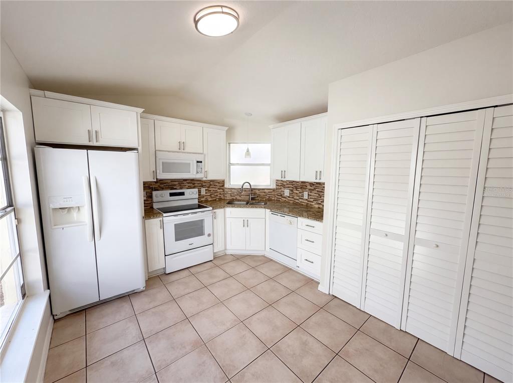 A kitchen features white cabinets, white appliances, tile flooring, and a brown tiled backsplash — 9814 DEAN COVE LANE, ORLANDO, FL