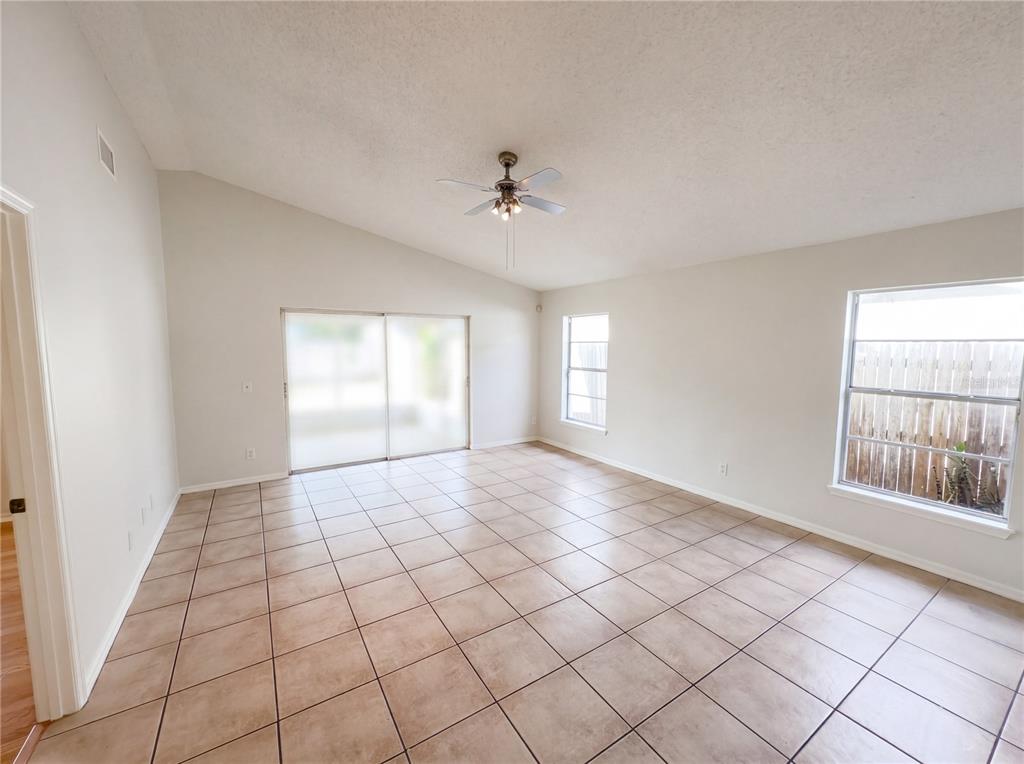 An empty living room features beige tile flooring, a vaulted ceiling, and sliding glass doors — 9814 DEAN COVE LANE, ORLANDO, FL