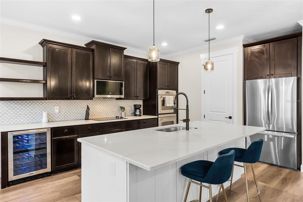 A modern kitchen features dark wood cabinets, a white island with blue stools, and stainless appliances — 2915 W BAY VIEW AVENUE, TAMPA, FL