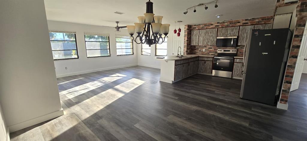 An open-concept kitchen and living area features wood-look flooring, brick accents, and a large chandelier — 1174 VICTORIA AVENUE, PORT CHARLOTTE, FL