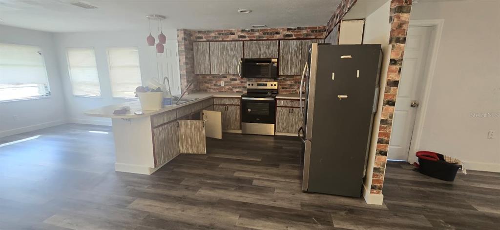 A kitchen features wood-look cabinets, a brick backsplash, stainless steel appliances, and wood-plank flooring — 1174 VICTORIA AVENUE, PORT CHARLOTTE, FL