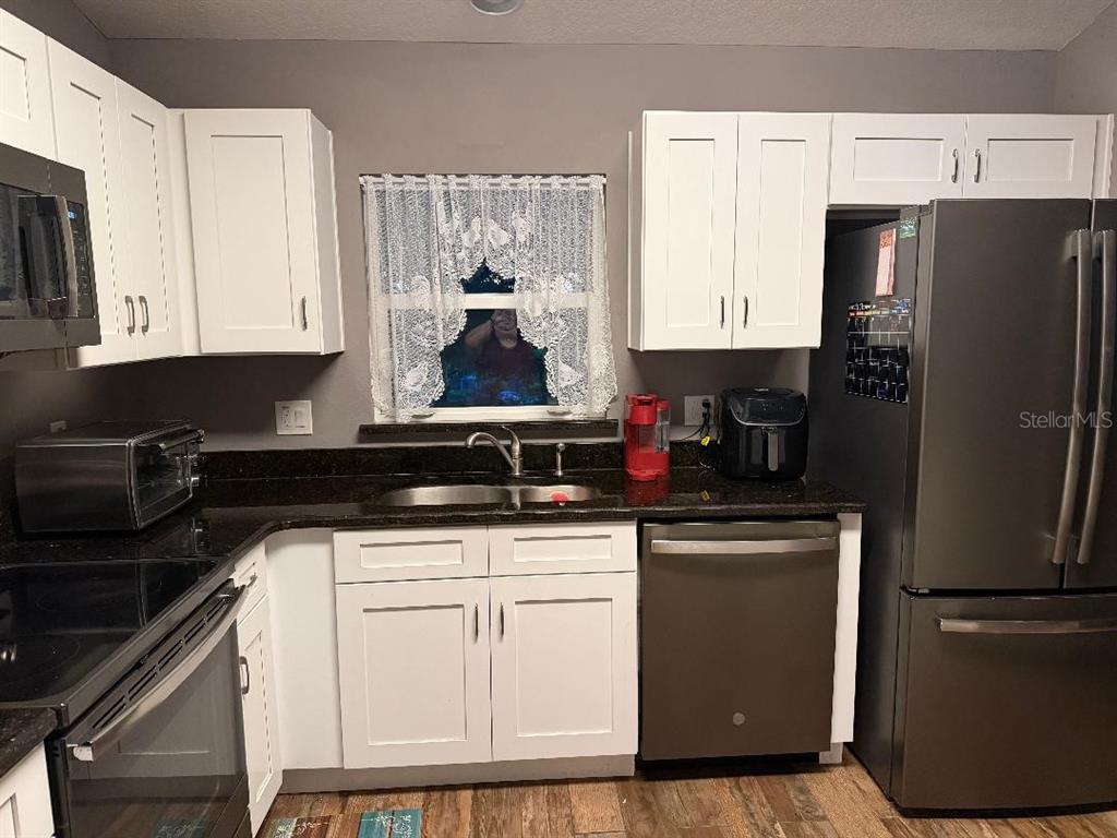 A kitchen features white cabinets, dark granite countertops, stainless steel appliances, and a window — 2212 GAMEWELL COURT, DELTONA, FL