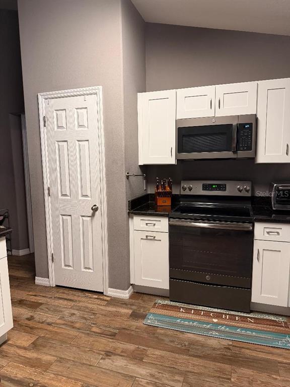 A kitchen features white cabinets, black appliances, dark countertops, and wood-look flooring — 2212 GAMEWELL COURT, DELTONA, FL