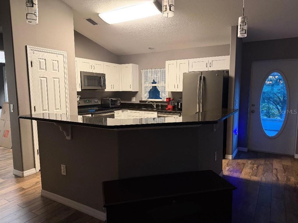 A kitchen with white cabinets, dark countertops, and a breakfast bar overlooking a living area — 2212 GAMEWELL COURT, DELTONA, FL