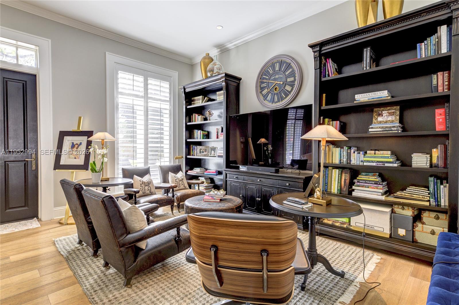 A living room features dark wood bookshelves, leather armchairs, a television, and a large wall clock — 641 Almeria Ave, Coral Gables FL 33134, CORAL GABLES, FL