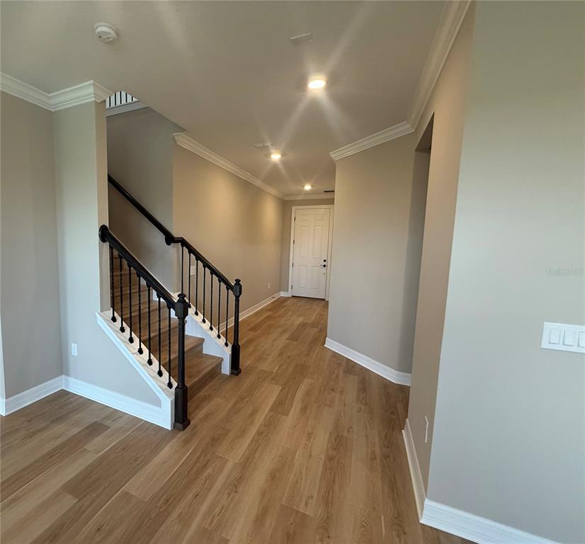 An entryway features light wood-look flooring, a staircase with a black railing, and a white door — 455 WINTER GROVE BOULEVARD, WINTER GARDEN, FL
