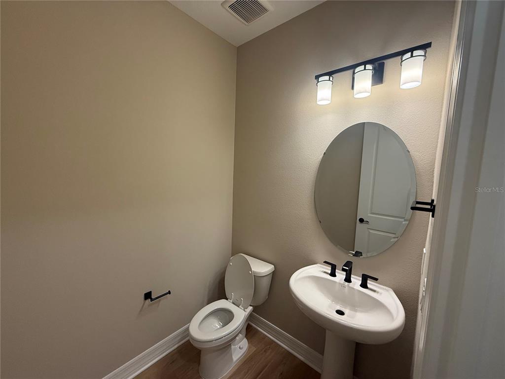 A half bathroom features a pedestal sink, a round mirror, and a toilet on wood flooring — 455 WINTER GROVE BOULEVARD, WINTER GARDEN, FL