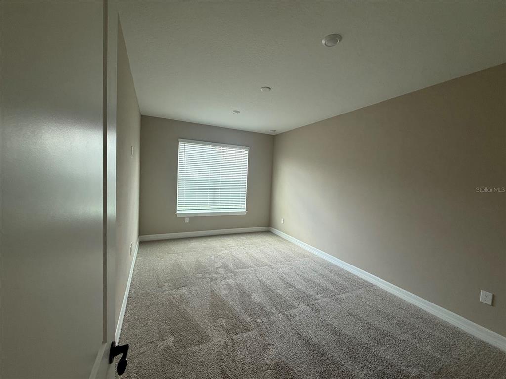 An empty bedroom features beige walls, neutral carpeting, and a single window with white blinds — 455 WINTER GROVE BOULEVARD, WINTER GARDEN, FL