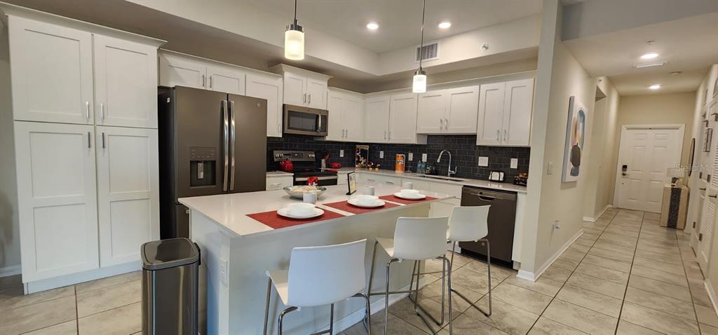 A kitchen features white cabinets, a central island with bar seating, and stainless steel appliances — 3150 PARADOX CIRCLE UNIT 302, KISSIMMEE, FL