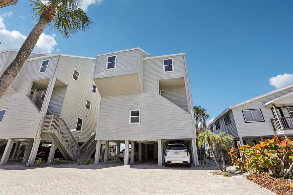 A low-angle exterior view of elevated, light-gray coastal townhomes with covered parking underneath — 19930 GULF BOULEVARD UNIT 3B, INDIAN SHORES, FL