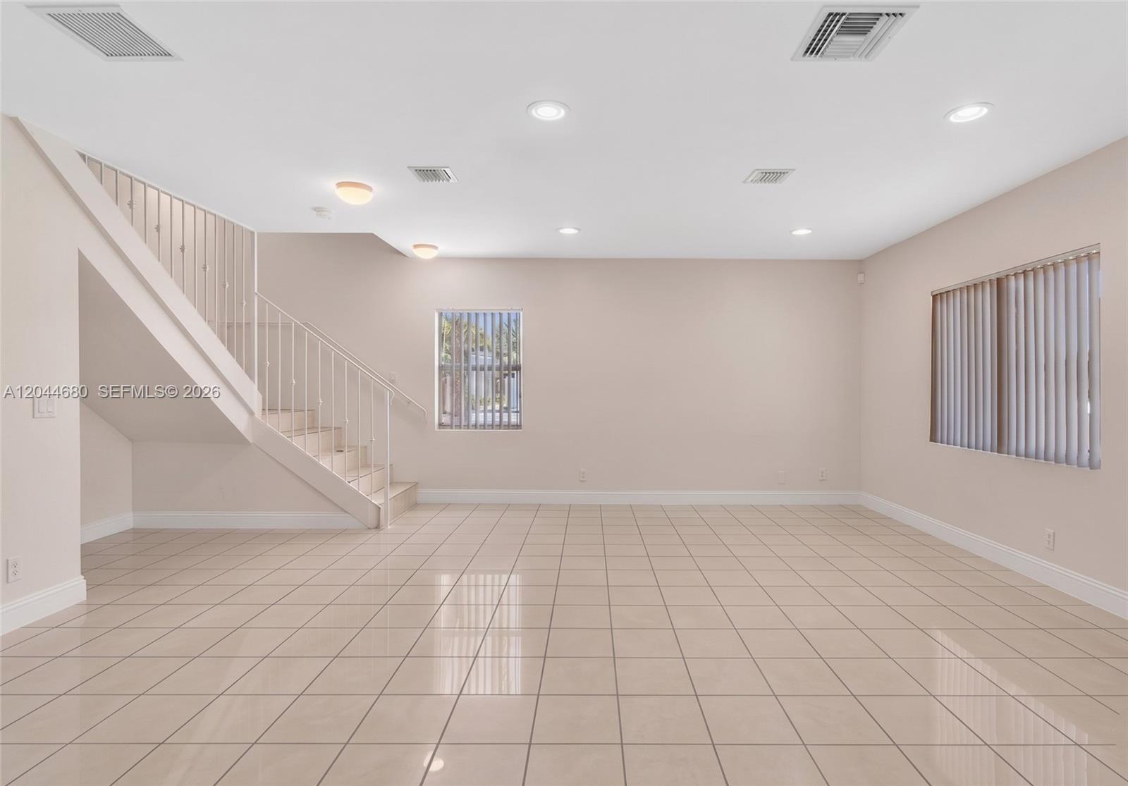 An empty room features beige tile flooring, a staircase with white railings, and two windows — 1316 NW 3rd St, Fort Lauderdale FL 33311, FORT LAUDERDALE, FL
