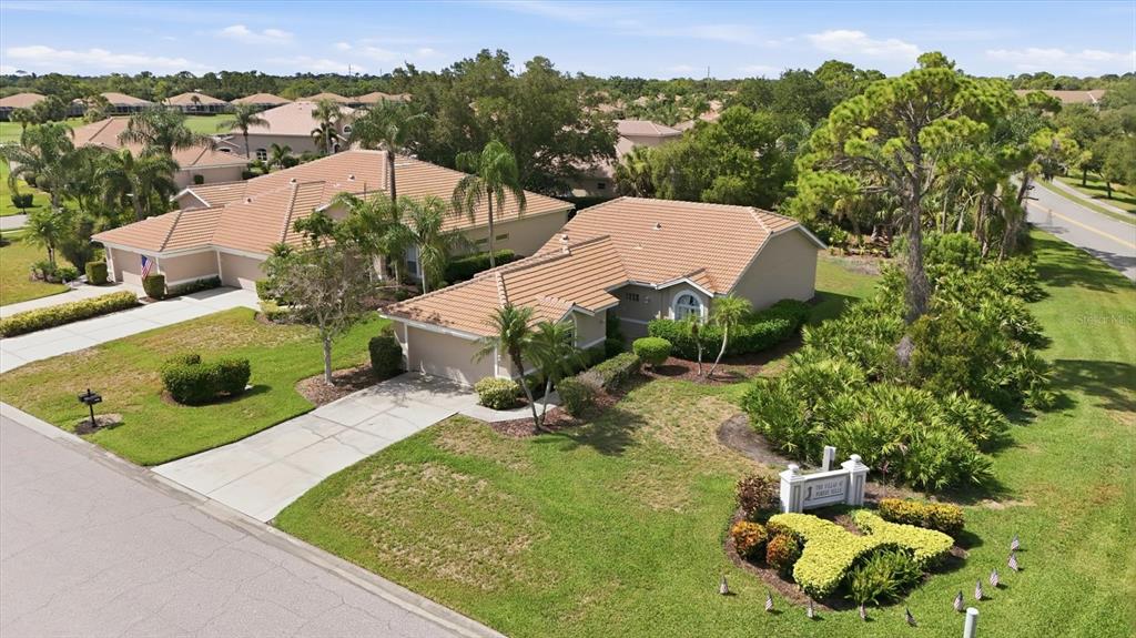 An aerial view shows a tan villa with a tiled roof and a landscaped entrance sign — 9402 FOREST HILLS CIRCLE, SARASOTA, FL