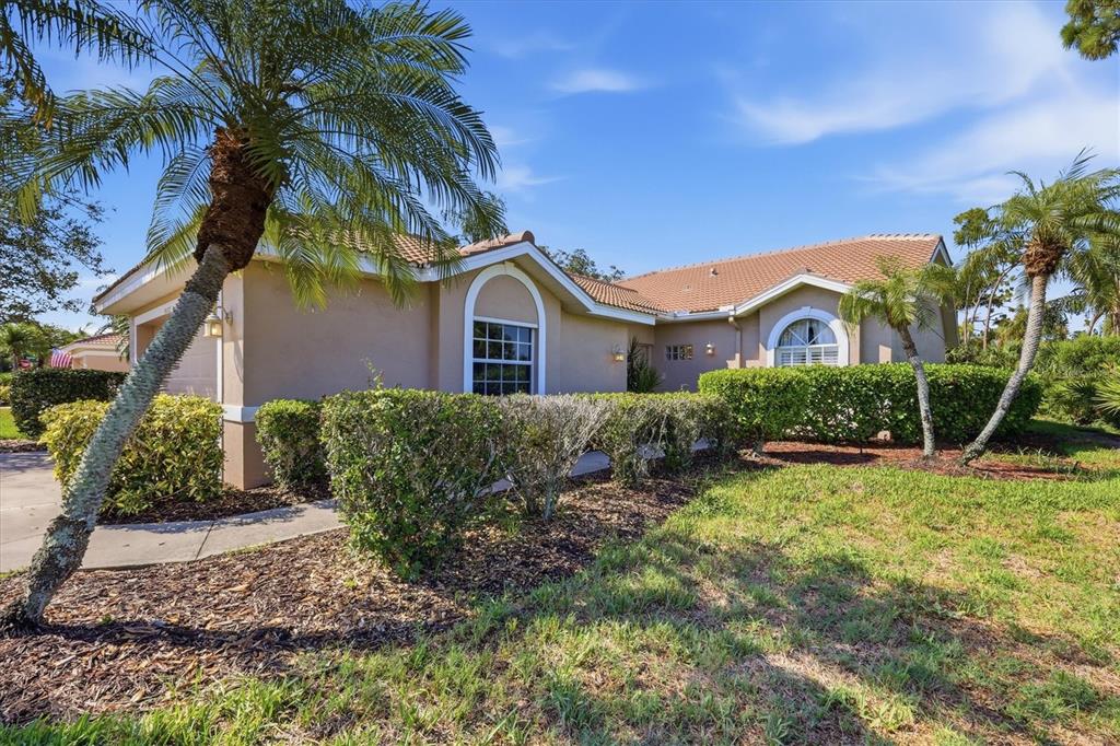 A single-story tan house with a tiled roof, arched windows, and palm trees in front — 9402 FOREST HILLS CIRCLE, SARASOTA, FL